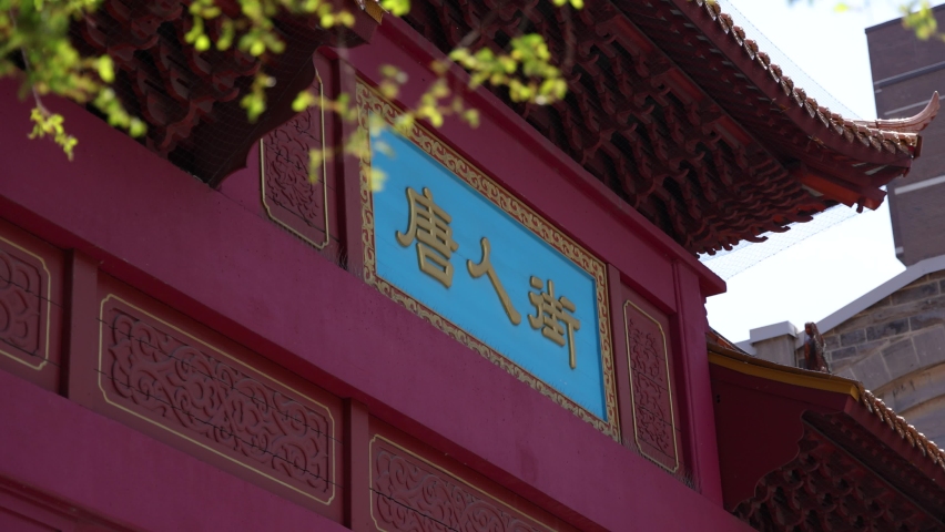 Slow motion camera panning footage showing the oriental architectural elements of the paifang gate entrance to Chinatown over a street in Montreal.