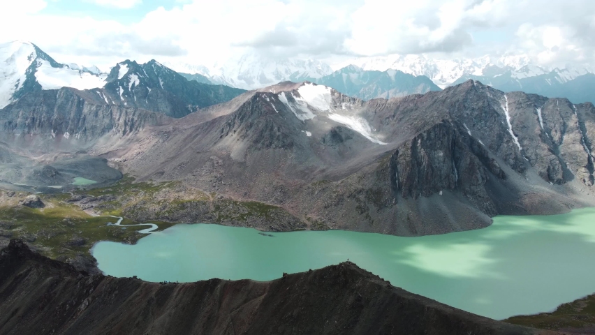 Man in red stay on edge of cliff. Ala-Kul Lake in Issyk Kul Region in Kyrgyzstan. Drone footage 4K. Mountains with big lake and epic clouds.  | Shutterstock HD Video #1093289087