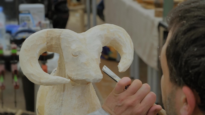 Man carpenter, wood sculptor using chisel for carving wooden sculpture of goat - slow motion, close up. Carpentry, craftsmanship, design and hobby concept