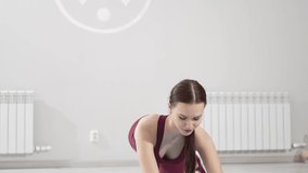 a woman in a burgundy tracksuit does leg exercises with gymnastic elastic bands on a mat. video and online lessons for sports. clothes and shoes for gymnastics. professional fitness trainer. 