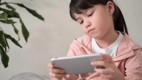 Cute little kid girl holding smart phone enjoying using mobile apps, playing games at home. Small child learning in cellphone, watching video. Mobile technology concept. 