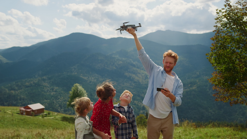 Happy family using drone on walk summer mountains. Red hair man launching quadcopter from hand outdoor. View of modern quadrocopter flying in cloudy sky operating by young guy. Technology concept. Royalty-Free Stock Footage #1093293919