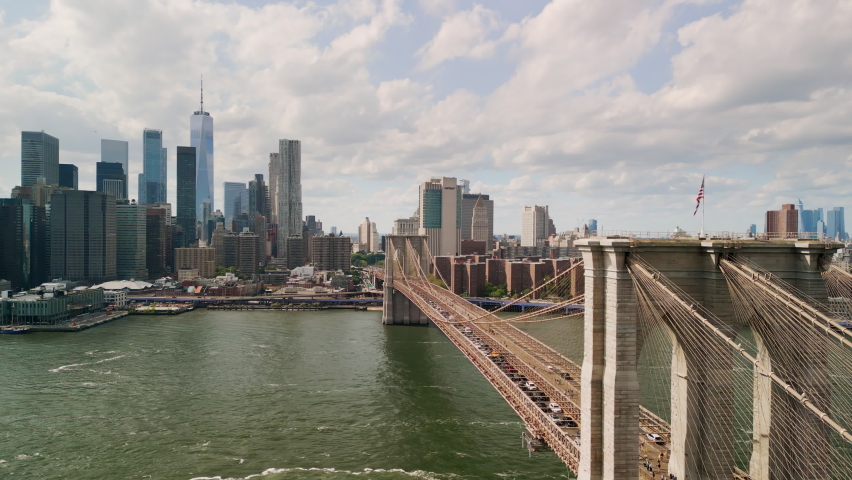 AERIAL Flight over Brooklyn Bridge with American flag and East River view over Manhattan New York City Skyline  | Shutterstock HD Video #1093299201