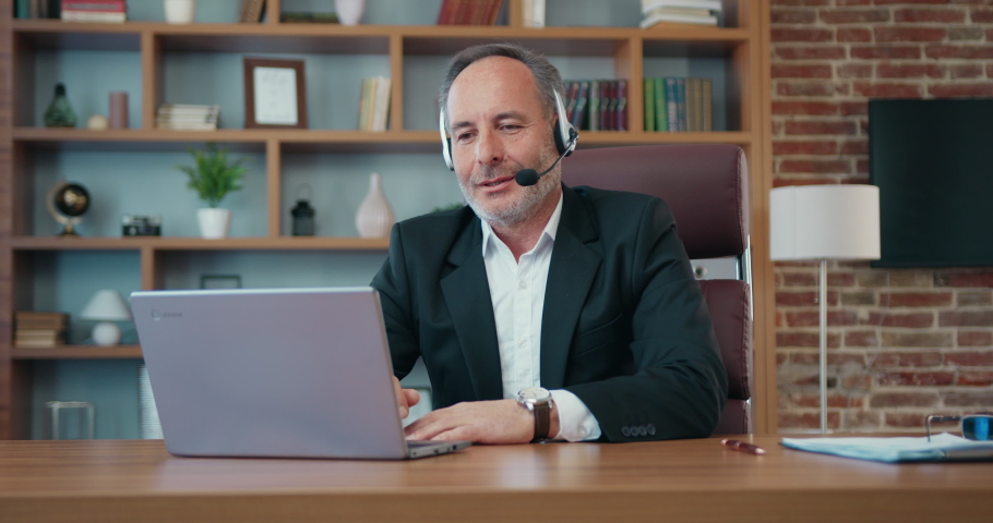 Attractive positive successful bearded businessman in headset holding videochat on computer with his business partners in modern office Royalty-Free Stock Footage #1093312729