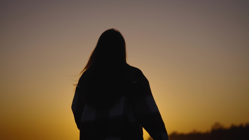 The silhouette of a beautiful and slender woman against the backdrop of the sunset sky.