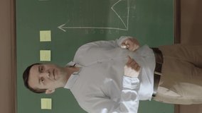 A businessman or teacher is explaining graphics to employees or students in front of a blackboard. The manager gives seminars to the employees, draws chalk charts on the blackboard, answers questions. - Powered by Shutterstock - Get 15% off with code: PIKWIZARD15