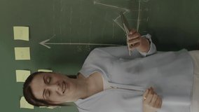 Female teacher explaining math to students in front of blackboard with chalk notes and math formulas. She tries her best to help her students succeed in their future lives.Vertical video.