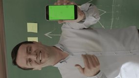 Male teacher in front of blackboard looking at information on the phone, searching for something on the Internet, reading news.Businessman pointing his smartphone with green screen to the camera.