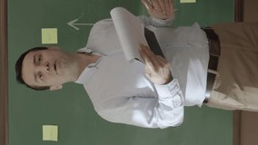 The male teacher looks at his notes in front of the blackboard, reads the reports to his students, presents them to staff or students. Giving a thumbs up sign that everything is perfect.Vertical video