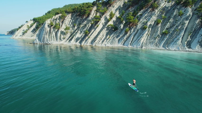 Men on stand up paddle board in blue sea. Surfer on SUP board with incredible landscape. Aerial view