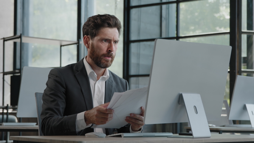 Adult bearded Caucasian angry businessman tired unhappy mad man sit at desk feel stress with paperwork deadline upset trouble with work throwing papers hate job nerves difficult startup worry | Shutterstock HD Video #1093323957
