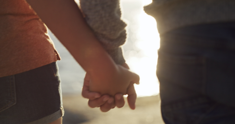 Romantic, in love couple holding hands on the beach showing love, affection and care enjoying a beautiful sunset sea view. Romance closeup of a boyfriend and girlfriend bonding together by the ocean