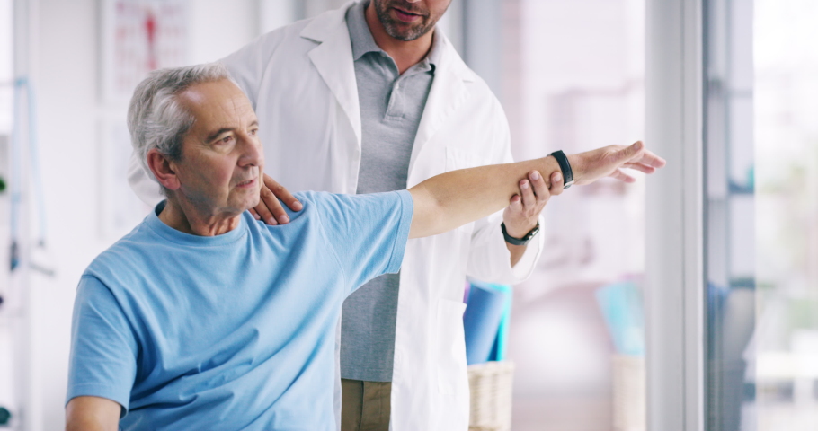 Physiotherapist stretching a senior man with shoulder pain and massaging his arm in a clinic to help him. A male chiropractor doing a treatment on a mature or old guy by doing an exercise Royalty-Free Stock Footage #1093325951