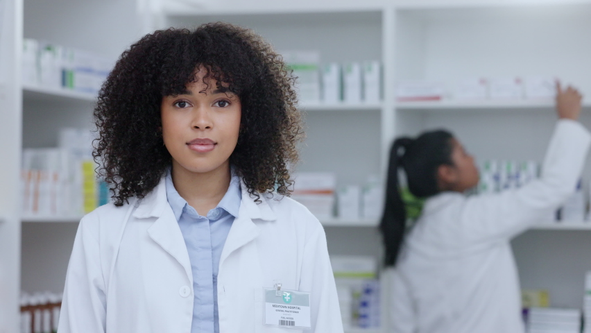 Pharmacist, healthcare worker or medical student doctor smiling in a pharmacy. Young, happy and cheerful afro clerk standing with medicine and pills for patients pain, healing and wellness behind Royalty-Free Stock Footage #1093328111