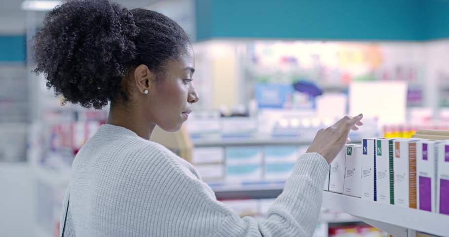 Woman looking at medicine in a box at a pharmacy, buying medication and reading information label. Happy black female browsing a wellness shop for illness treatment, health vitamins and pills | Shutterstock HD Video #1093328137