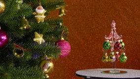 On a colored background, a small Christmas tree rotates near a beautiful decorated Christmas tree