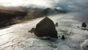 Aerial drone flying over Haystack Rock, Cannon Beach, Oregon, USA. Dramatic cloudy sunny day. Ocean waves crashing. Rocky cliff. Coastline. High quality 4k footage