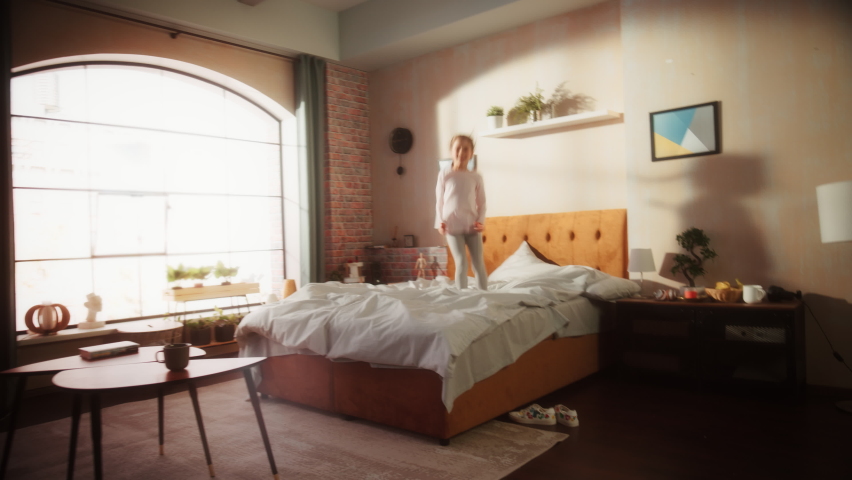 Mother and Small Daughter Having Fun at Home. Cheerfully Playing, Running Around and Jumping on a Bed in Stylish Loft Apartment. Happy Childhood, Parenthood and Motherhood Memories. Royalty-Free Stock Footage #1093337813