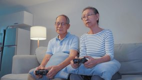 Asian happy family play console game together in living room at night. Senior elderly older couple grandparent sitting on sofa, feel excited and enjoy spend time play joystick gaming activity in house