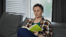Young pretty woman reading book while sitting on sofa at home