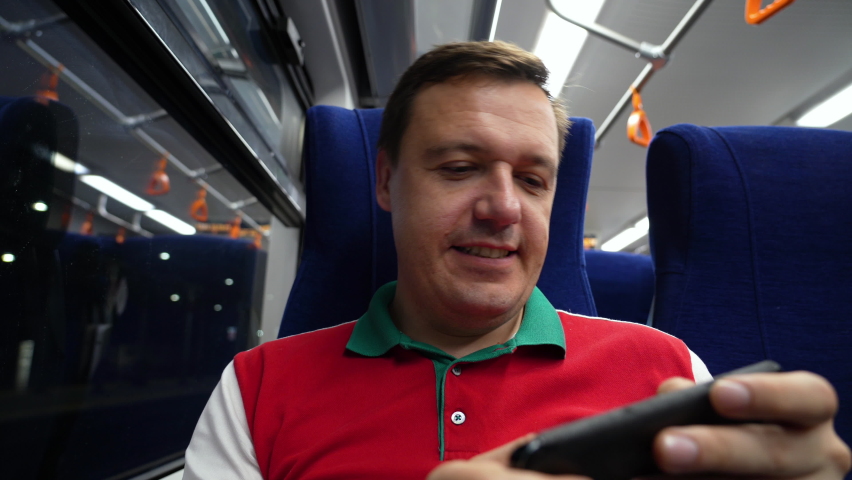 Caucasian millennial man excited playing mobile game on 5g smartphone in metro. Gambling man cheering and playing racing app on mobile phone while riding in public transport.