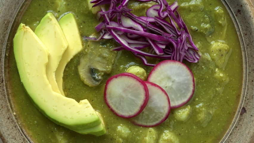 Green Pozole Verde dish with hominy, tomatillo, shredded jackfruit and button mushrooms with avocado, radish and red cabbage. Close-up of vegan pozole dish.