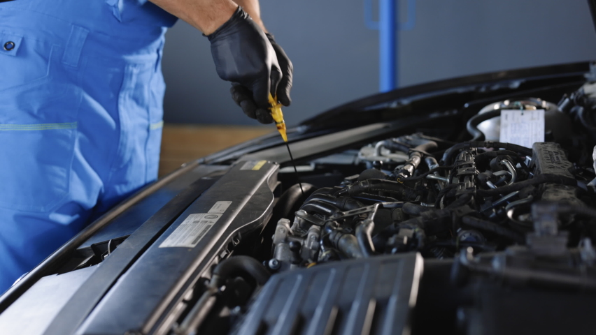 Close-up of automotive mechanic checks the oil level on the car engine dipstick. Car oil quality. Inspection of the engine and checking motor oil level. Man checks the car oil level with dipstick. | Shutterstock HD Video #1093345991