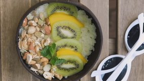 Vertical video. Top view of woman eating fresh organic rice porridge with tropical fruits and nuts, healthy vegetarian menu