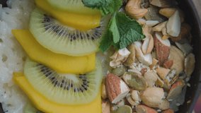 Vertical video. Morning rice porridge with slices of fruits and nuts on table, close-up. Balanced vegan diet concept