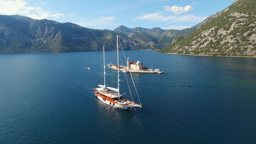 Sailing yacht sails past the island of Gospa od Skrpjela. Perast, Montenegro Royalty-Free Stock Footage #1093347335