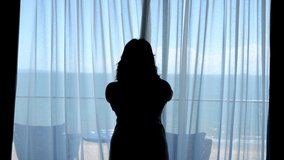 Slow motion video of a woman opening a curtain in a sea view room.
