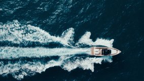 Top view slow motion drone shot of luxury motorboat in ocean waters near marina. Panning shot of yacht swim and raise waves in open blue waters. Amazing epic background over waves in sea