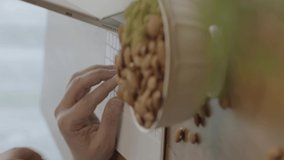 A freelance man drinks coffee, eats roasted almonds, hazelnuts, cookies while working remotely from his home. Close-up portrait of man's hands eating roasted almonds or hazelnuts.Vertical video.