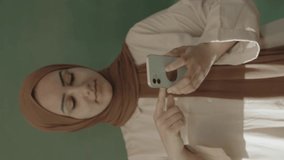 In the classroom,the teacher in hijab looks at social media accounts with her smartphone,browses the internet,reads e-mails,surprised by what she sees and showing her green screen phone to the camera.