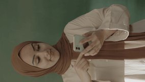 In the classroom,the teacher in hijab looks at social media accounts with her smartphone,browses the internet,reads e-mails,surprised by what she sees and showing her green screen phone to the camera.