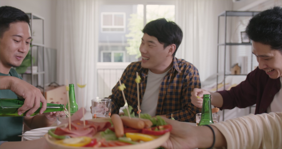 Happy hour good warm summer time diner indoor home. Group of asia people young adult friend man and woman sit at dining table joy fun talk or eat food and drink beer alcohol bottle glass inside house.