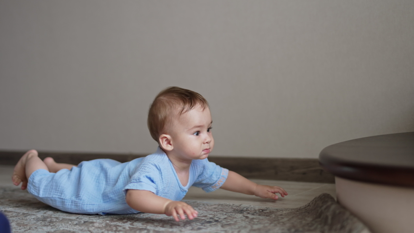 Cute adorable baby in blue romper crawls by the floor to the stairs. Beautiful child wants to get a toy from the stair. | Shutterstock HD Video #1093368893