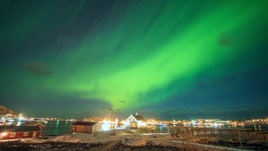 Time lapse of Beautiful aurora borealis, Northern lights over illuminated fishing village on arctic ocean coastline at Lofoten Islands, Norway