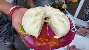 A man is holding a steamed Bao which is sold in the food stall in  TIRETTA BAZAR, Kolkata, on a paper plate served with red spicy sauce. No face video