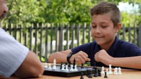 Elderly man and child play chess at table in park. Grandfather teaches his grandson to play board game in yard. - Powered by Shutterstock - Get 15% off with code: PIKWIZARD15