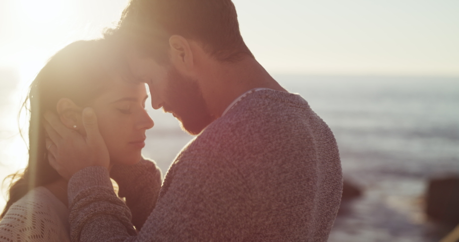 Romantic, in love and hugging young couple sharing a loving sweet moment, spending quality time and bonding on a beach during a sunset with flare. A man and woman on a relaxing date by the ocean Royalty-Free Stock Footage #1093375079