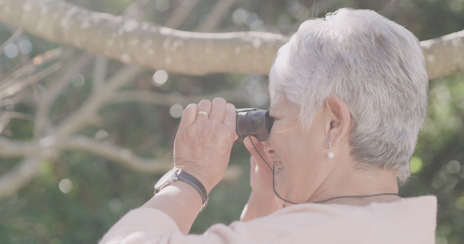Binoculars, hiking and freedom with a senior woman enjoying birdwatching, exploring and adventure in nature. Closeup of a mature female looking at the view while taking a outdoors hike in the forest | Shutterstock HD Video #1093375173