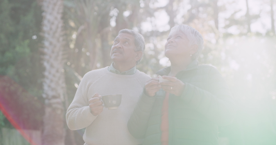 Mature couple enjoying retirement, laughing and bonding outside while drinking coffee, tea and hot drink. Senior woman talking, pointing and showing elderly man in a home garden, backyard and yard | Shutterstock HD Video #1093375181