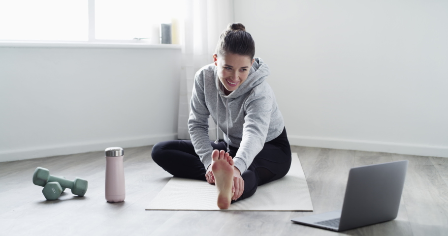 Fit, active woman vlogging, live streaming or teaching an online workout on a laptop at home. Healthy female fitness, exercising, doing cardio stretching or yoga while on a video call indoors | Shutterstock HD Video #1093375187