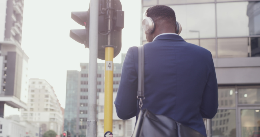 Fun businessman enjoying listening to music and walking in modern corporate business area. Young African American male enjoying motivation audio in urban city downtown after successful day at work | Shutterstock HD Video #1093375303