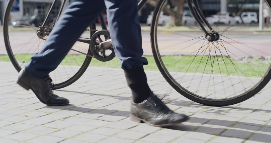 Business man walking in city with bike, commuting to work or traveling in morning routine in town. Closeup legs or feet of entrepreneur in travel, trip or commute with eco friendly transport | Shutterstock HD Video #1093375313