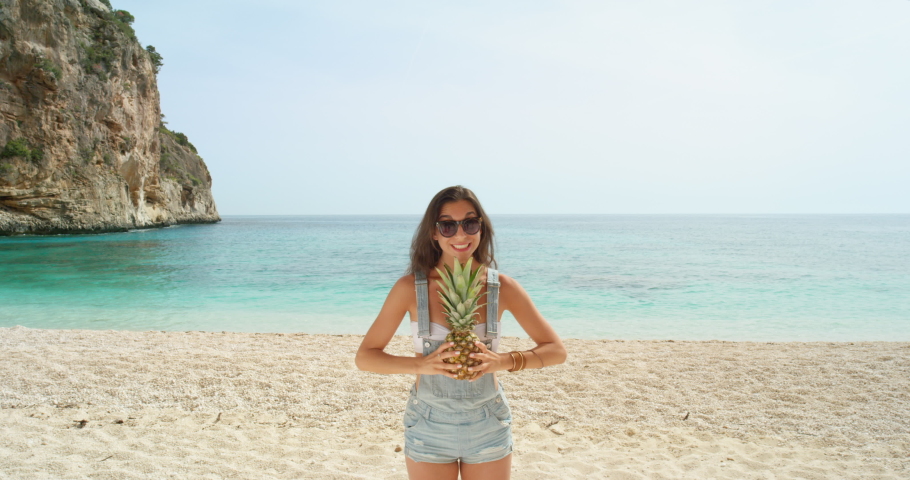 Tropical woman with a pineapple on head for balance, carefree and healthy lifestyle on a vacation, holiday or getaway with beach or sea background and copy space. Fun, slim tourist with summer fruit | Shutterstock HD Video #1093375329