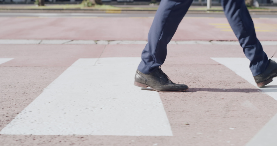 Closeup of feet walking over a public crossing, zebra cross and urban street in a city or town. A casual male walk on white lines during a green light and follow road rules and safety outside | Shutterstock HD Video #1093375331