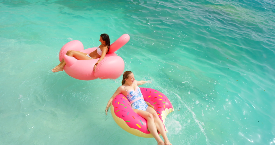 Vacation, friends and summer travel while floating on clear blue water and enjoying the water while splashing and having fun. Above young women relaxing on inflatable tube at beach and holiday | Shutterstock HD Video #1093375345