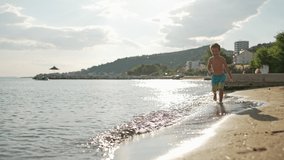 A slow-motion video of a child, a boy running on the water of the sea and splashing from it. A happy smiling child on vacation near the ocean is happy and having fun. High quality 4k footage